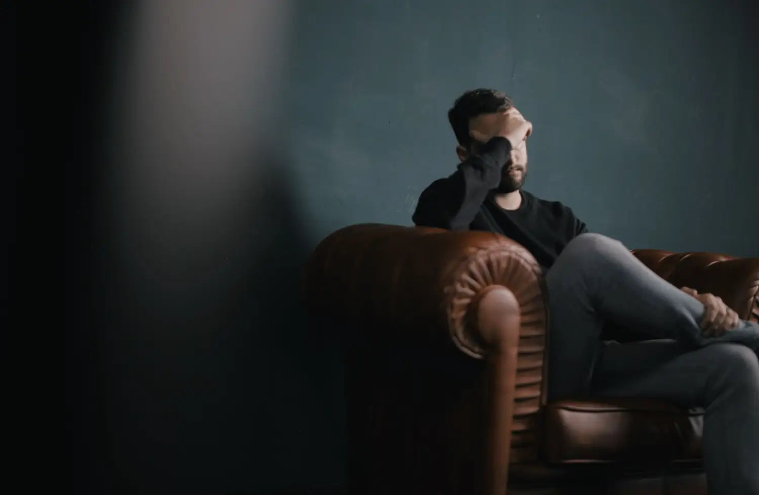 Man sitting on couch holding his head in his hands.