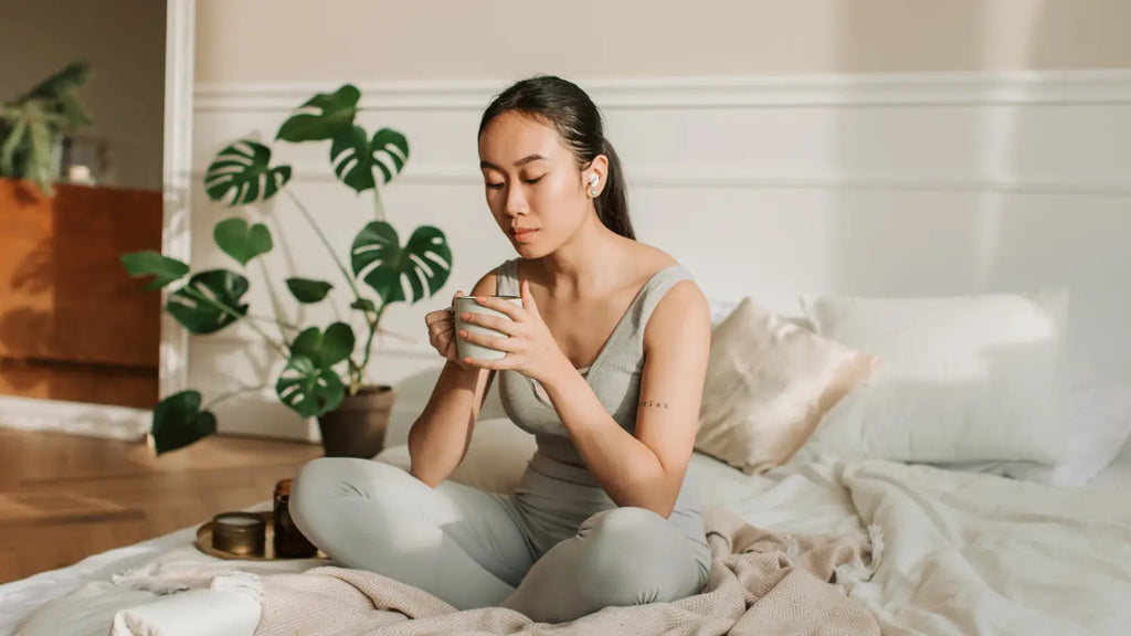 Woman drinking tea while sitting on bed