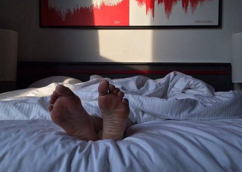 Feet appearing at the end of a bed.