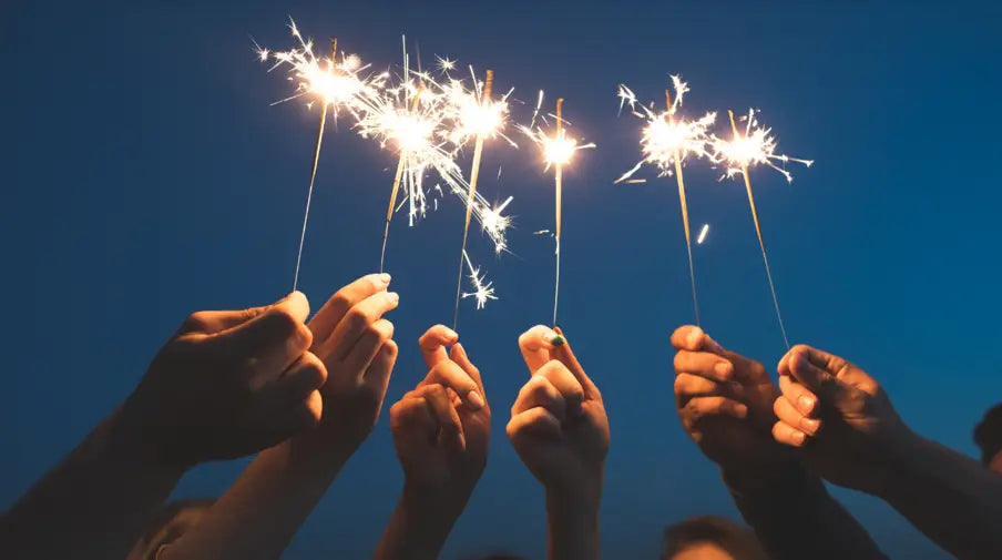 Friends celebrating new year by holding sparklers against the sky