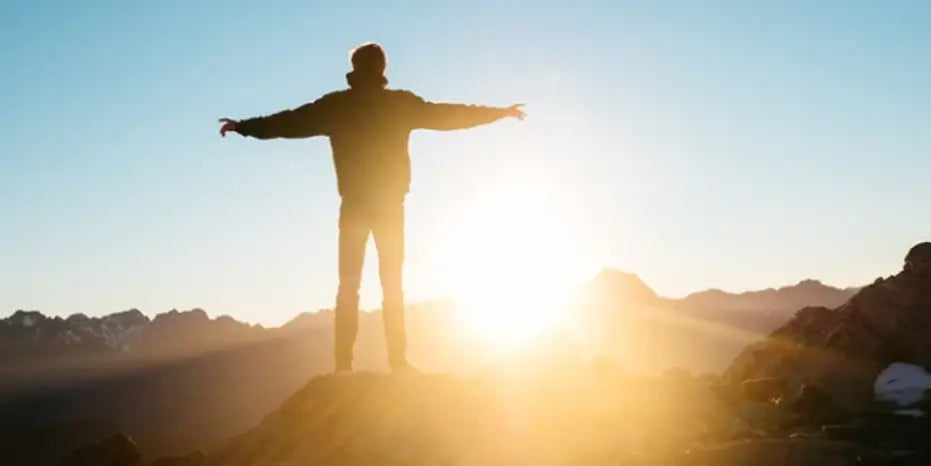 Man with open arms on top of hill during sunset