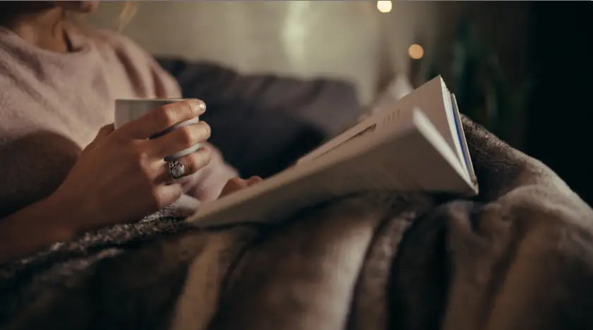 Woman reading book and drinking tea while in bed