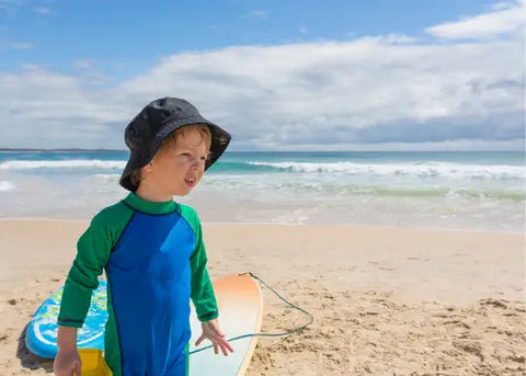 Kid on the beach wearing protective clothingand hat.