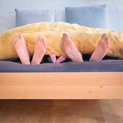 Feet of a couple and a child appearing at the end of a bed.