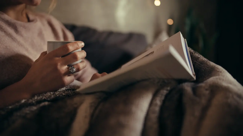 Woman reading a book and holding a cup of tea on bed