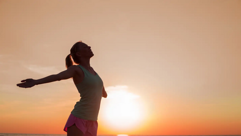 Woman with open arms in front of sunset