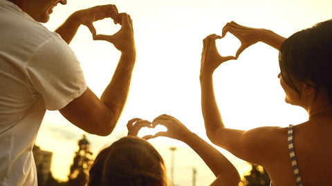 Hands of family in the shape of a heart against the sunset.