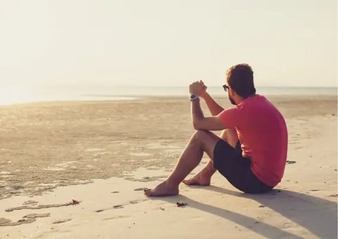 Man at the beach, sitting in the sand.