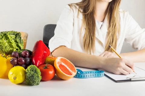 Woman writing in notebook on table with healthy foods and measuring tape.