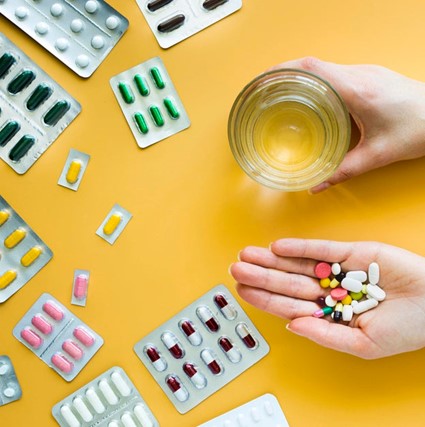 Person holding various pills and a cup of water.