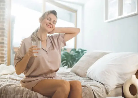 Woman drinking water sitting on the bed.