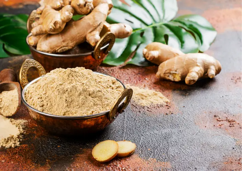 Fresh ginger root and ginger powder in a copper bowl.