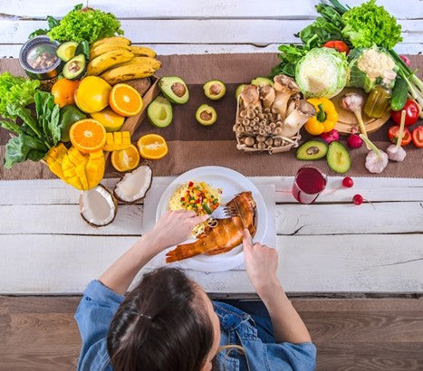 Woman eating a healthy meal at a table with vegetables and fruits.