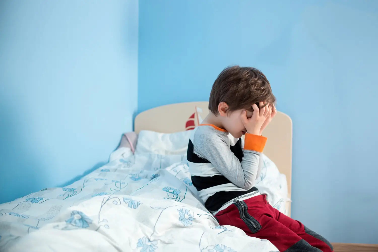 Kid sitting in bed holding his head in his hands.